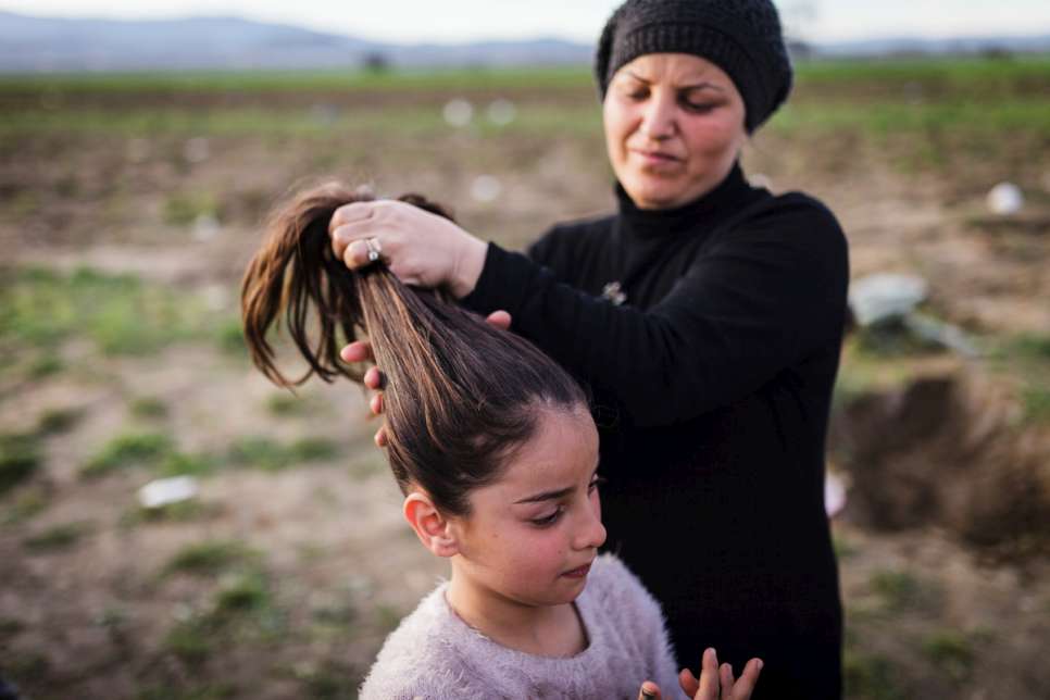Nisrine helps her daughter Adiba, 11, with her hair in the middle of a field where the family has set up a small camping tent along with other refugees.