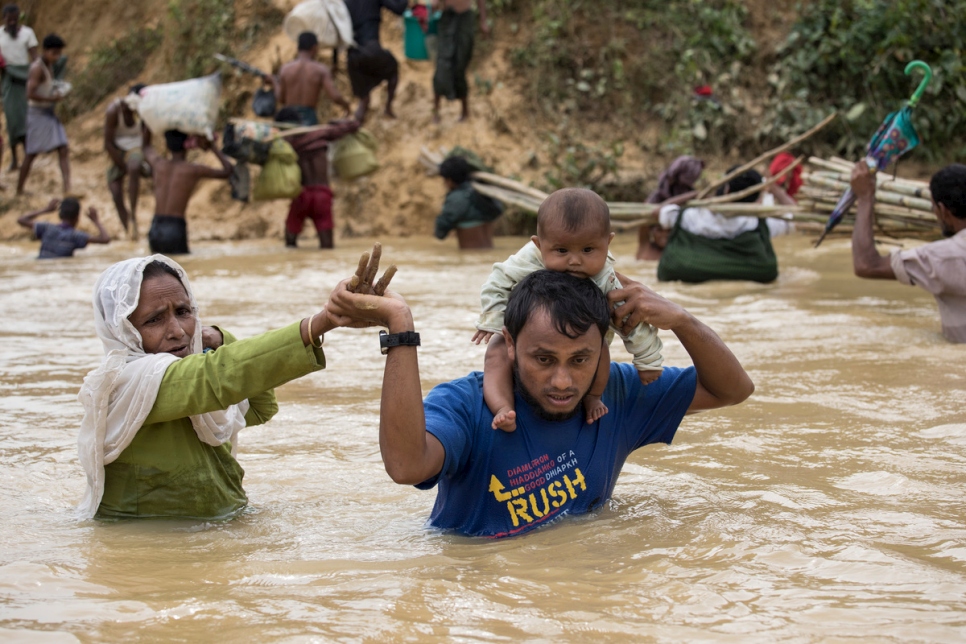 عائلة من اللاجئين الروهينغا من ميانمار تعبر نهراً فائضاً بسبب الأمطار الموسمية في كوتوبالونغ، بنغلاديش، خلال موسم المطار الموسمية في عام 2017.