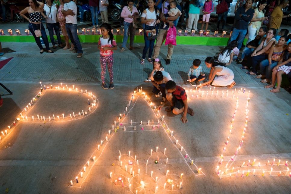 نساء وأطفال يضيئون الشموع لرسم كلمة "باس" (أي السلام) في حدث مجتمعي من تنظيم اتحاد "حائكات" النسائي في موكوا، كولومبيا.
