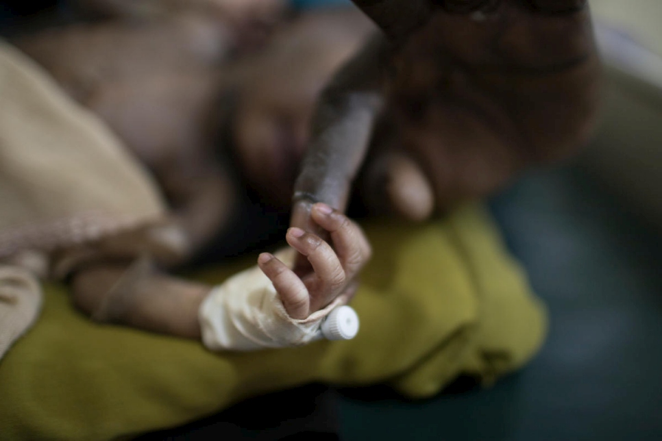 Un nouveau-né réfugié saisit le doigt du Dr Evan Atar Adaha à la maternité de l'hôpital de Bunj, au Soudan du Sud. 