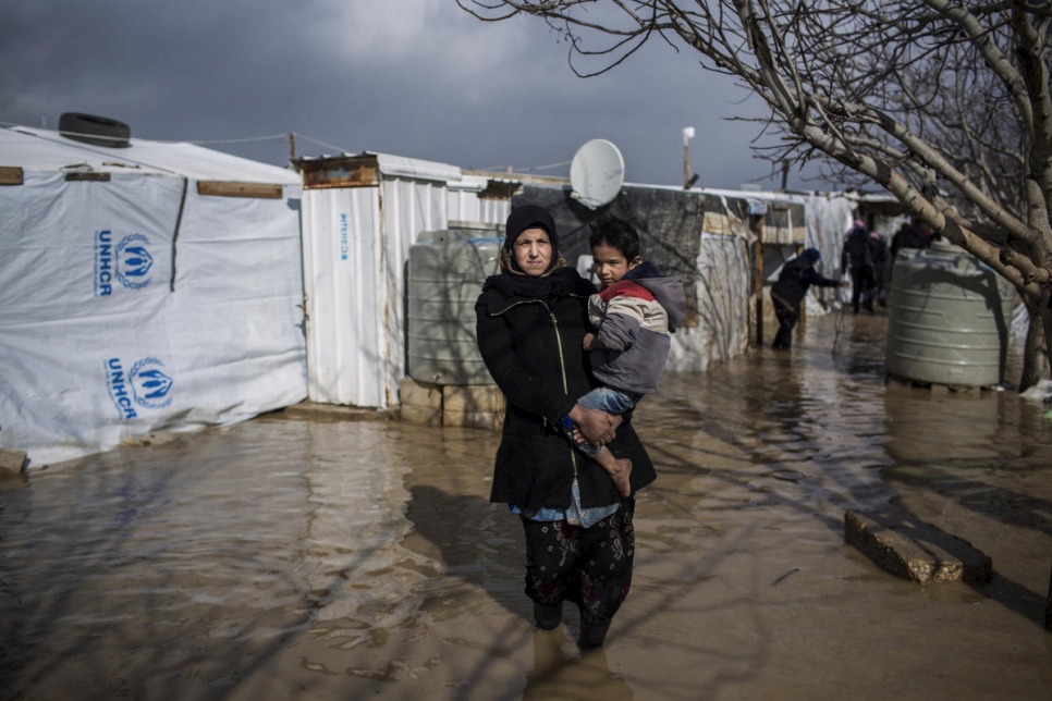 لاجئة سورية تحمل أحد أبنائها السبعة خارج منزل العائلة الذي غمرته مياه الفيضان في مخيم الدلامية العشوائي في سهل البقاع ، لبنان.
