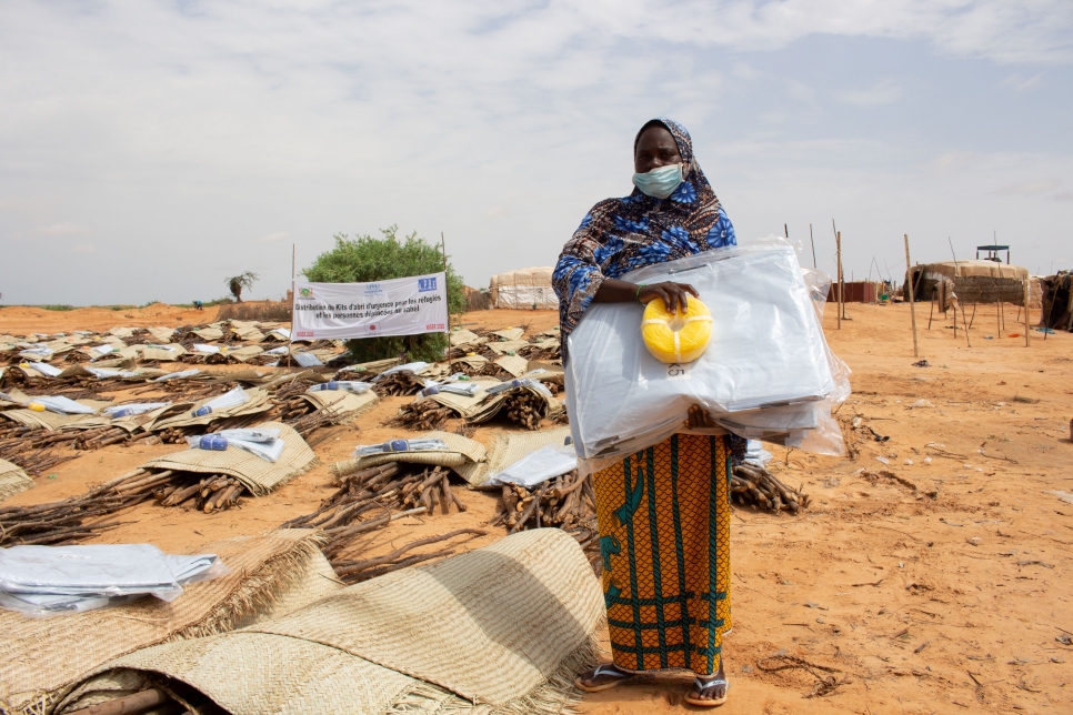 Aïssa Modi, une déplacée nigérienne âgée de 35 ans et mère de quatre enfants, se tient près d'un point de distribution de bois de chauffage sur un site de Zarmaganda, à Ouallam. Elle porte un kit d'abri distribué par le HCR. Il y a trois mois, elle avait fui le village de N'zouett, situé près de la frontière malienne, en quête de sécurité.  
