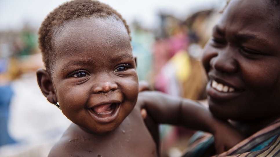 Seven-month-old South Sudanese refugee Gire Karyot, whose family was displaced from Kajo Keji, South Sudan, smiles as she is held by her mother at the Imvepi Reception Centre, Arua District, Northern Region, Uganda.