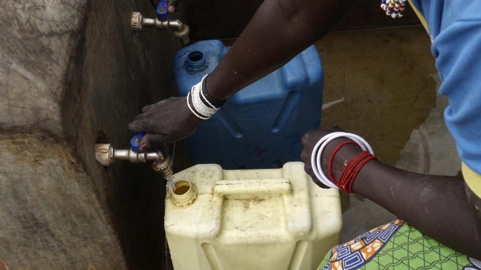 Des femmes de la communauté locale ougandaise remplissent des jerrycans à partir du point de distribution d'eau mis en place pour servir les réfugiés et leurs communautés hôtes autour de l'installation de réfugiés de Bidibidi. 