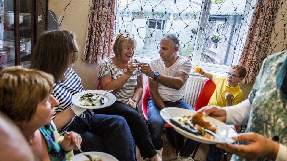 Ismael Khaled Jhayem offers stuffed vine leaves to Tricia Brophy, deputy chair of the Bishop Eton community group, at a meal for group members at the family's new home in Liverpool.