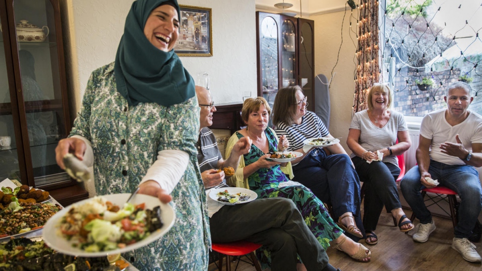 Ghofran Khaled Jhayem (left) and her husband Ismael (right) share Syrian food with members of their community support group at the family's new home in Liverpool.