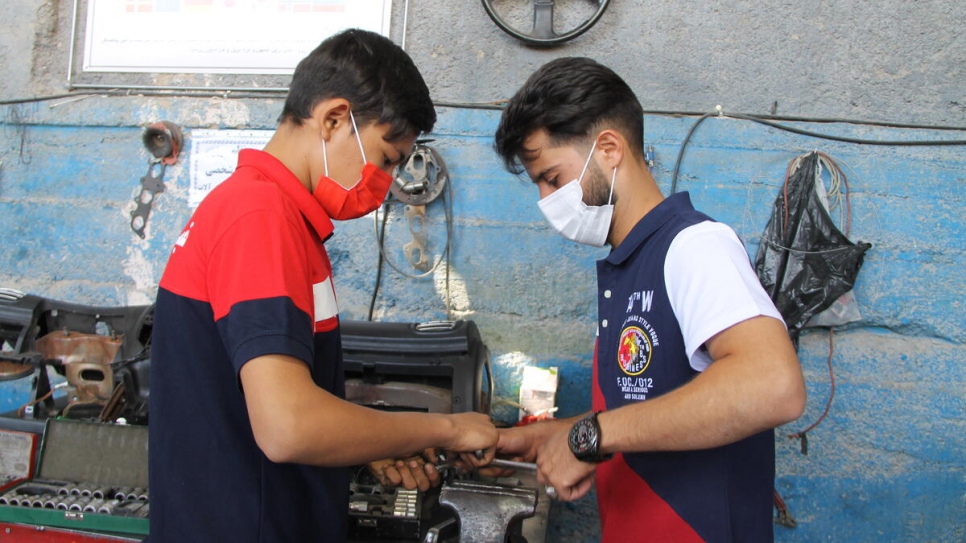 Iranian co-owner Danial Hosseini (right), 25, shows Soleiman (left), 18, how to repair an engine component.