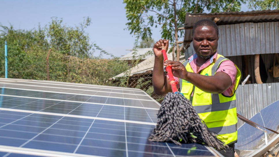 Vasco nettoie les panneaux solaires qui alimentent son mini-réseau électrique au camp de Kakuma. 