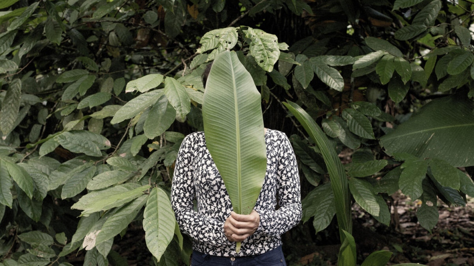 María*, a 28-year-old asylum seeker from Nicaragua who fled after her family received threats, poses for a portrait using a banana leaf to hide her identity.
