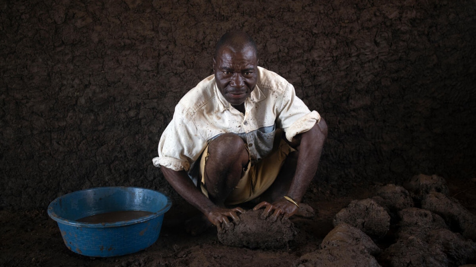 Patrício Alberto Mponda mixes water with mud that will be used to build the walls of his new home in Corrane site for displaced people. 