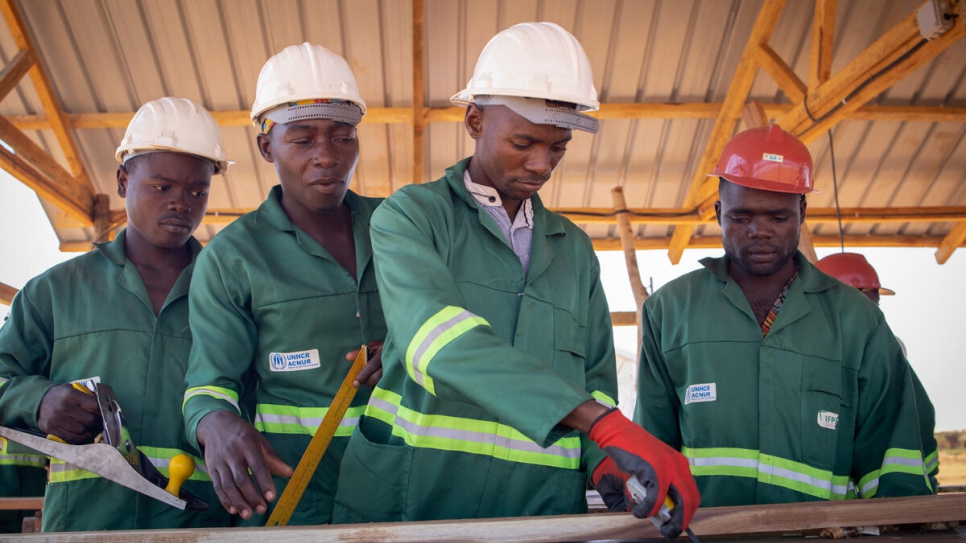 Des Mozambicains déplacés internes apprennent à fabriquer des planches pour les toitures afin de construire leurs propres abris au sein du camp de déplacés de Corrane, au Mozambique. 