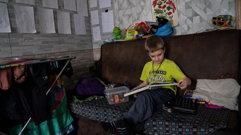 Ivan, 5, looks at a book in his great-grandparents' kitchen, where the Ukrainian alphabet has been stuck on the walls to help him learn.