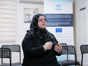 A person speaks in a community center, using hand gestures while sharing their experience.