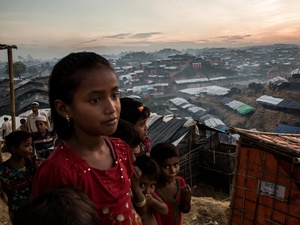 Young Rohingya refugees on a hillside at dusk overlooking a sprawling array of shelters.