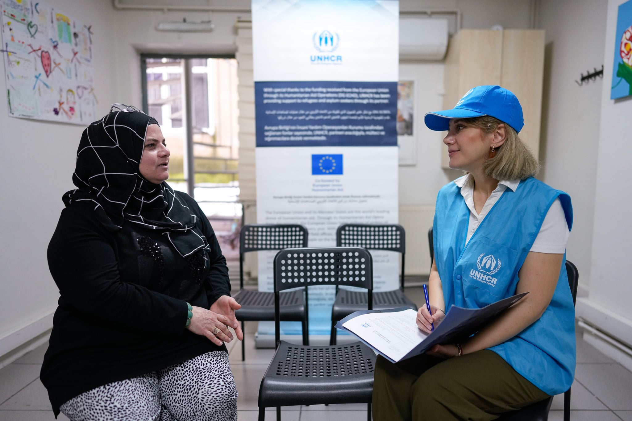 A UNHCR staff member conducts an interview with a person seated in a community center.