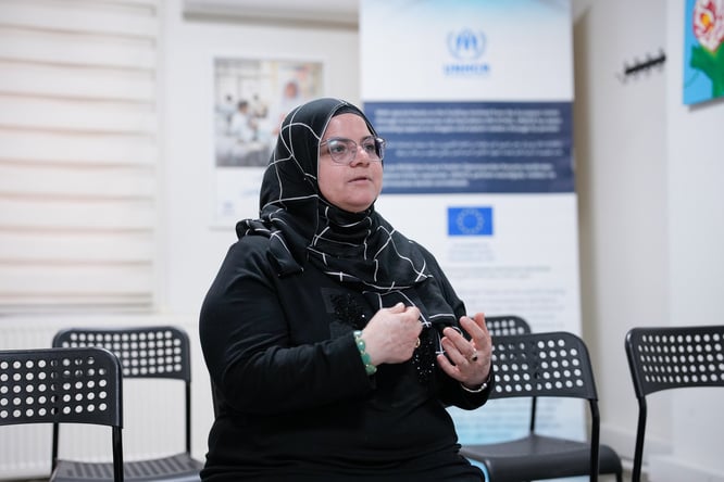 A person speaks in a community center, using hand gestures while sharing their experience.