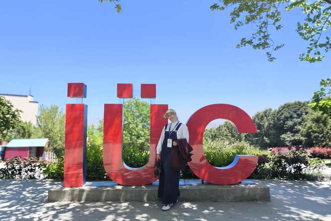 A person stands in front of large red “iuc” letters in an outdoor setting.
