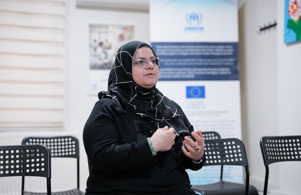 A person speaks in a community center, using hand gestures while sharing their experience.