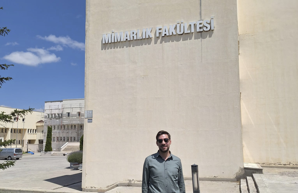 Person standing in front of a university Faculty of Architecture building on a sunny day.