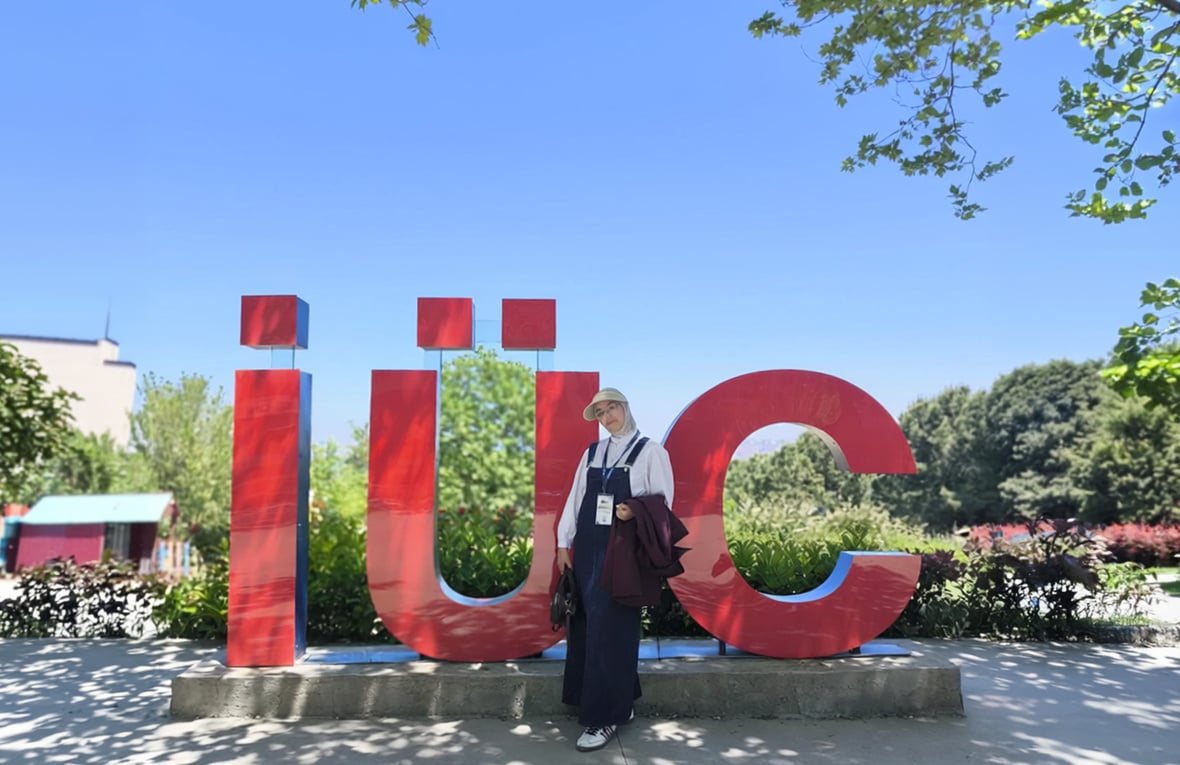 A person stands in front of large red “iuc” letters in an outdoor setting.