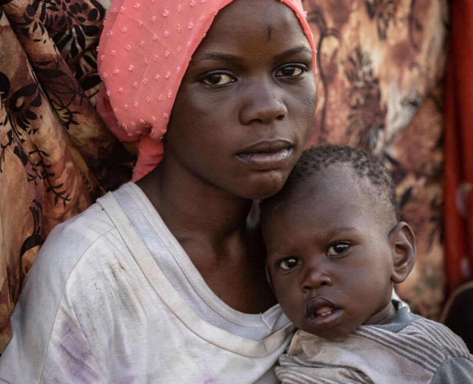 A young woman from South Sudan holds her one-year-old sister.