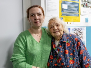A younger woman and an older woman stand together, arms around each other.