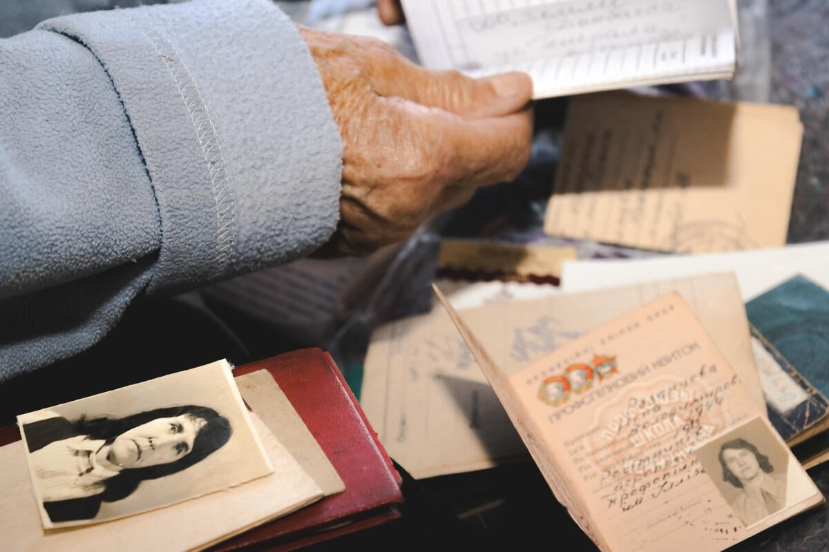 A hand holds a document while other documents and an old photo are spread out.