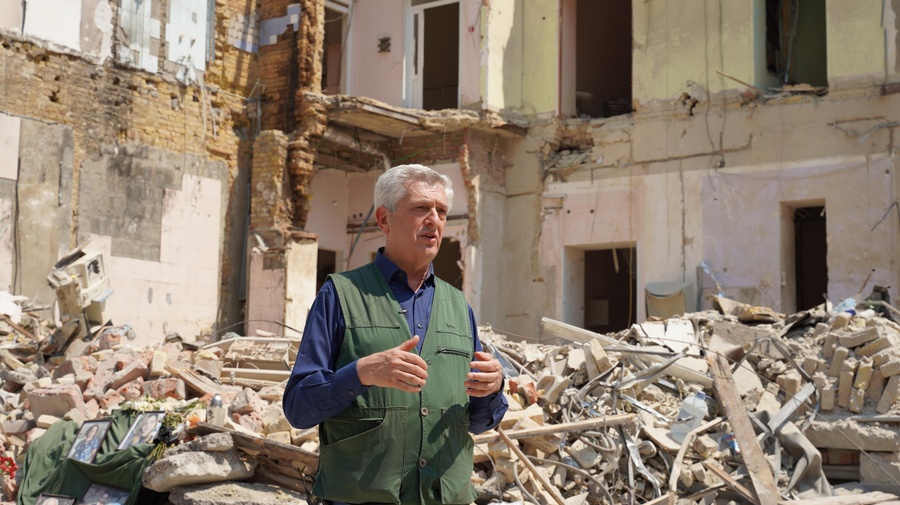 A man stands in front of the ruins of a heavily damaged building.