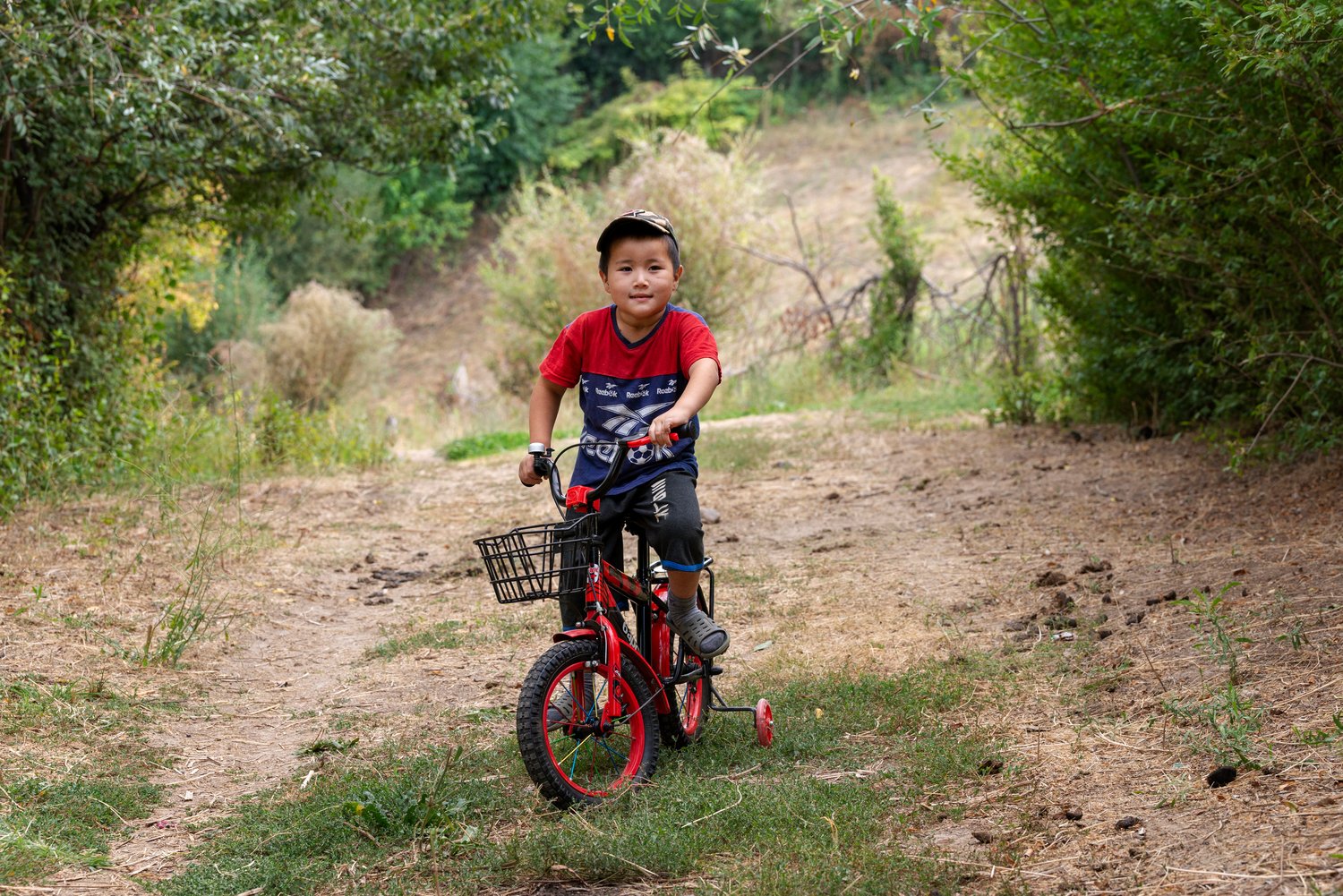 A young boy in a red t-shirt sits on his bike.