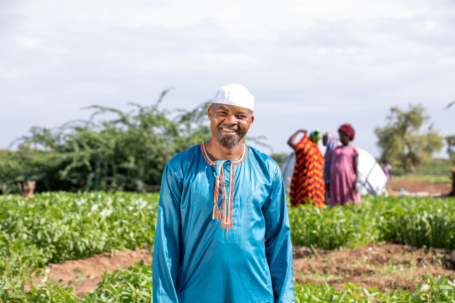 A smiling man stands in a field where crops grow.