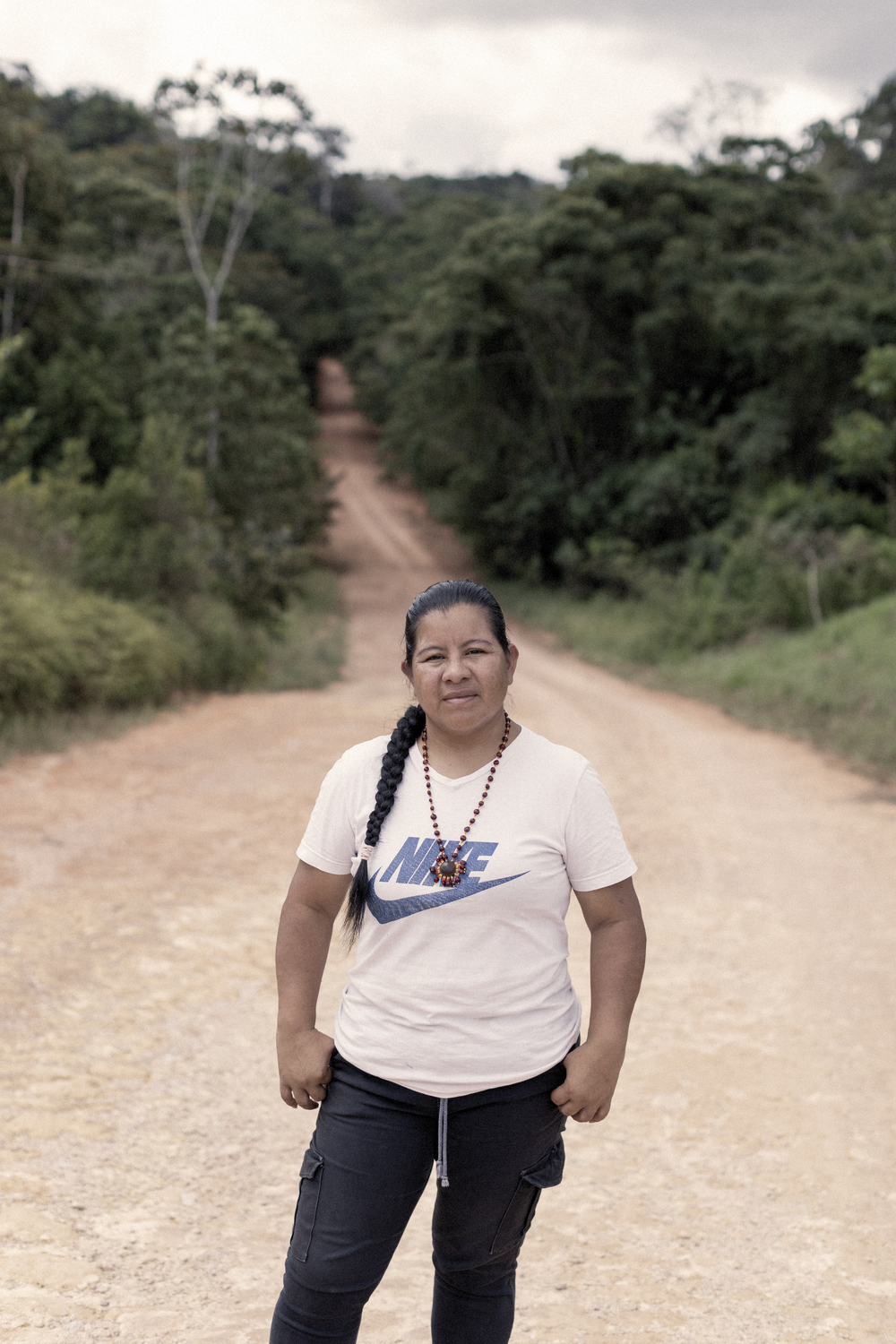 A woman stands in a dirt road that passes through a forest