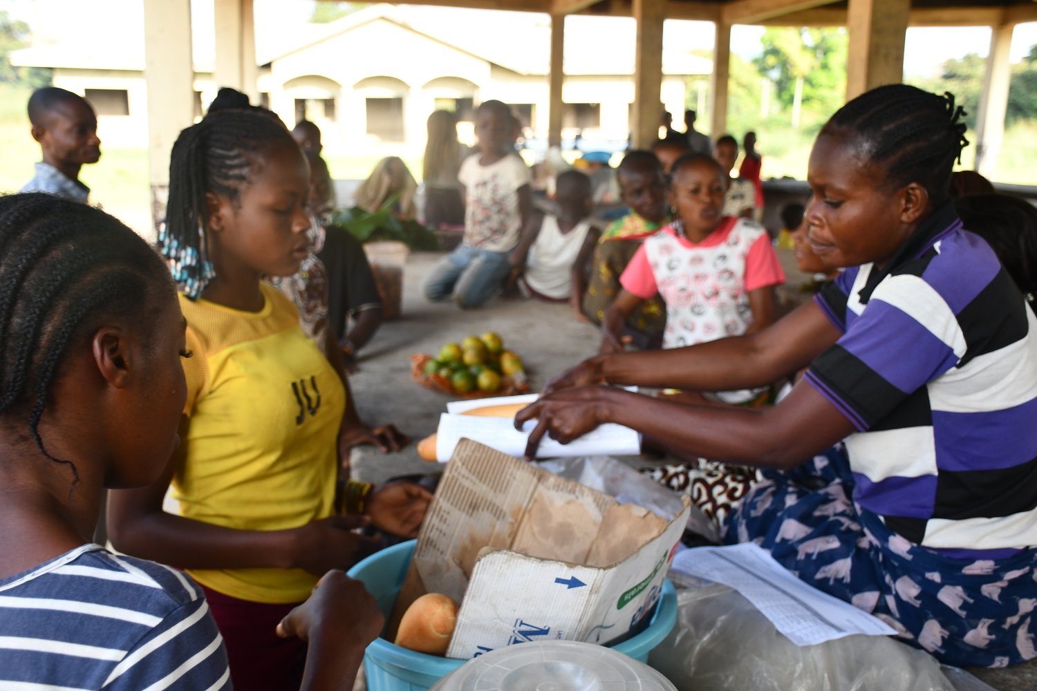 At a market, a woman hands over a small baguette wrapped in paper to a customer.