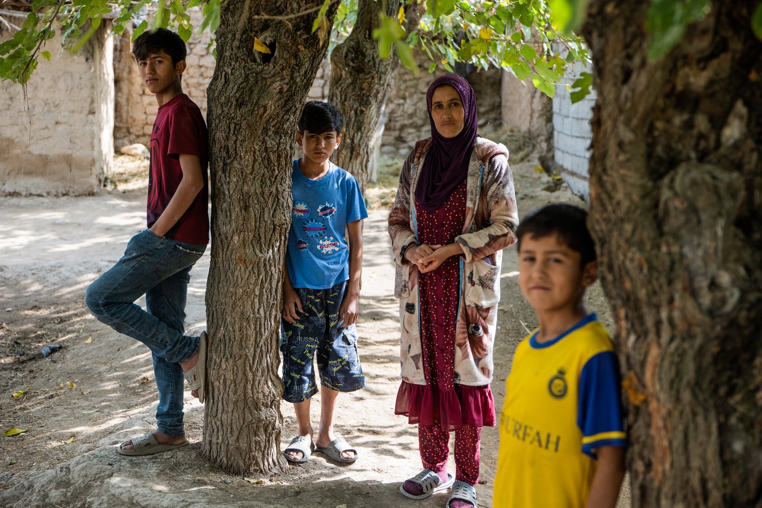 A woman stands amongst some trees with three boys of different ages.
