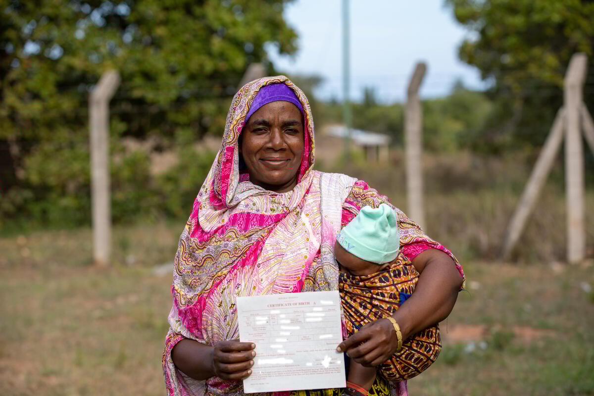 A Pemba woman from Kenya smiles while holding a baby in her arms, proudly displaying a document.