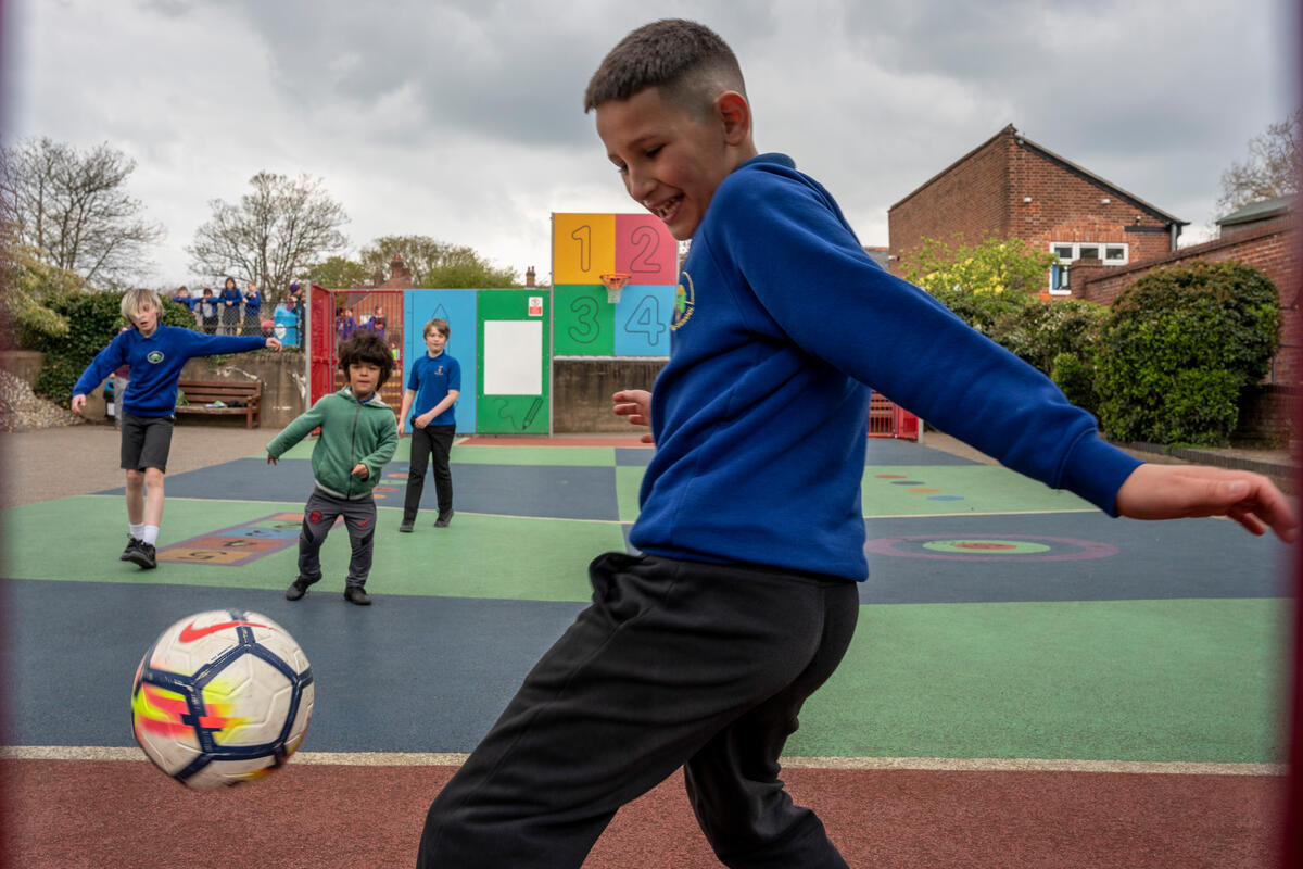 In a school playground a boy in uniform plays football.