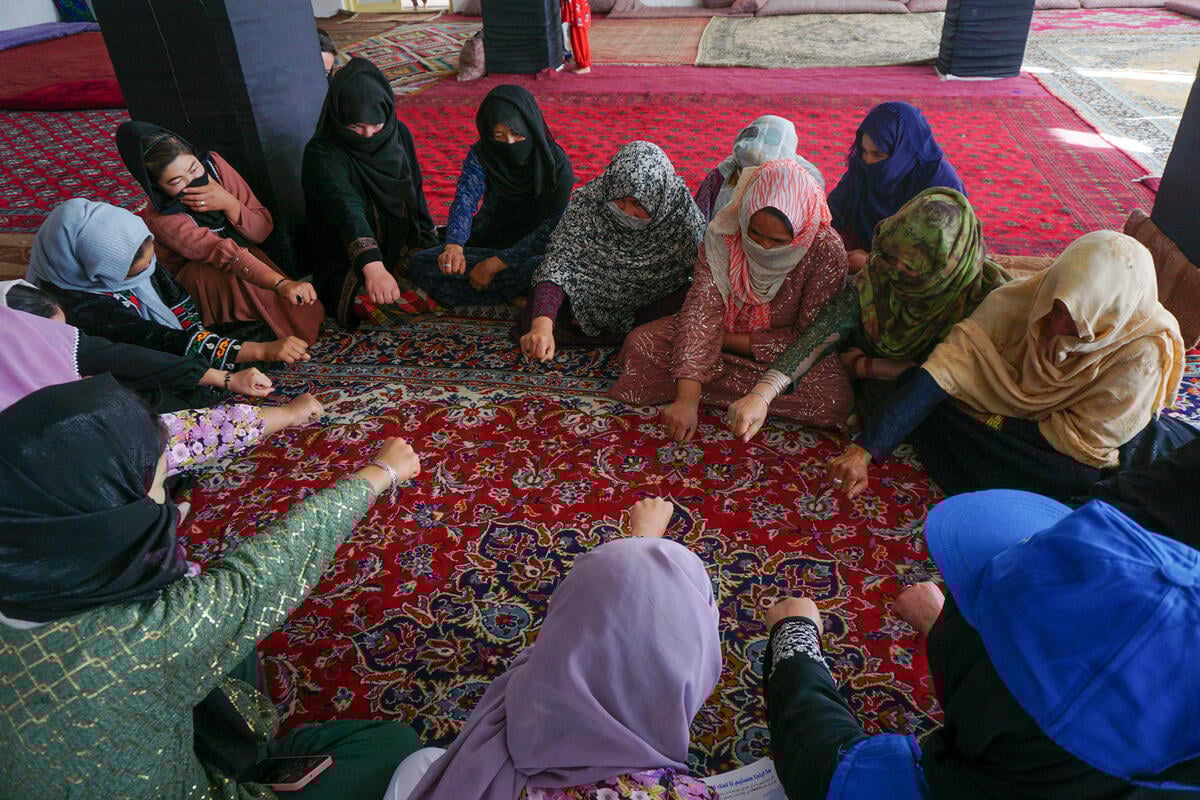 A group of women seated in a circle on a rug put their fists together.