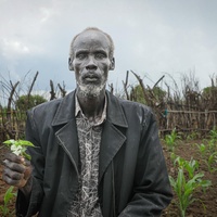 A South Sudanese man holds a plant in front of his field of crops