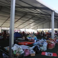 A temporary shelter filled with supplies and people in the background