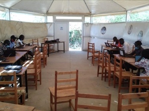 Estudiantes sentados en sus mesas colocadas dentro de una tienda blanca en el campamento de refugiados de Kakuma