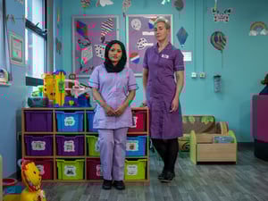 two women stand next to each other in a hospital ward