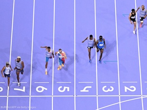An aerial view of four pairs of runners approaching the finish line of a running track.