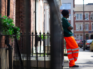 A person in orange trousers leans against a wall looking towards the street