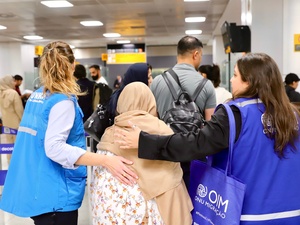 Staff from UNHCR and IOM walk through a crowded airport with their arms around a woman
