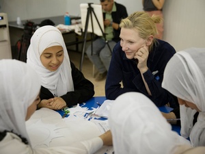 A smiling woman and four girls sit around a table holding scissors and paper 