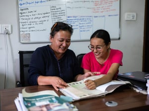 Two women smile as they page through some papers in a file.