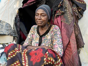 A woman sits in front of a makeshift shelter.