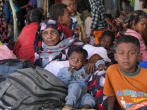 A woman sits on the floor surrounded by children and luggage