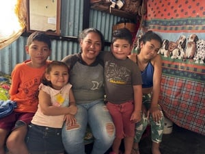 A mother sits on a bed in a shack with her four children.