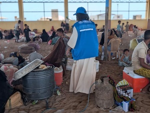 UNHCR staff support displaced families gathered in a large shelter with a sand floor
