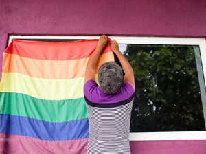 A person hangs a rainbow flag to a window.